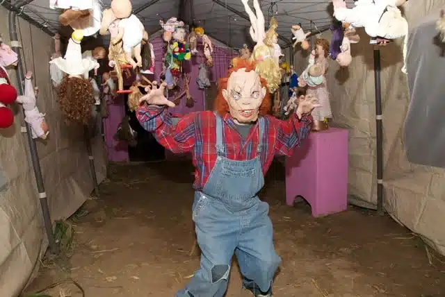 Creepy Character Standing in Haunted Attraction with Scary Dolls Hanging from the Ceiling at Tucson Terror in the Corn